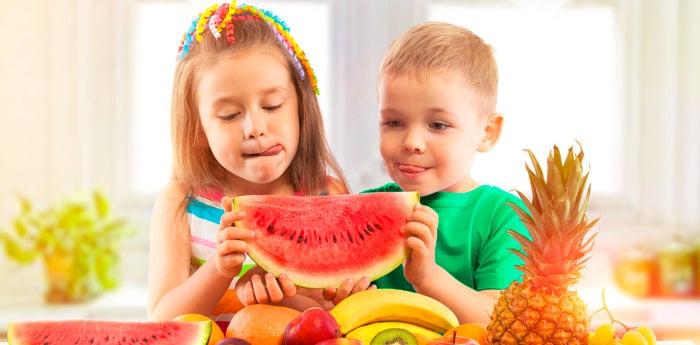 Niños saboreando una sandía junto a otros tipos de frutas