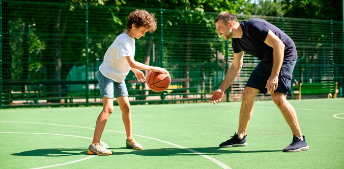 Papá jugando baloncesto con su hijo en una cancha aprovechando los beneficios de la actividad física