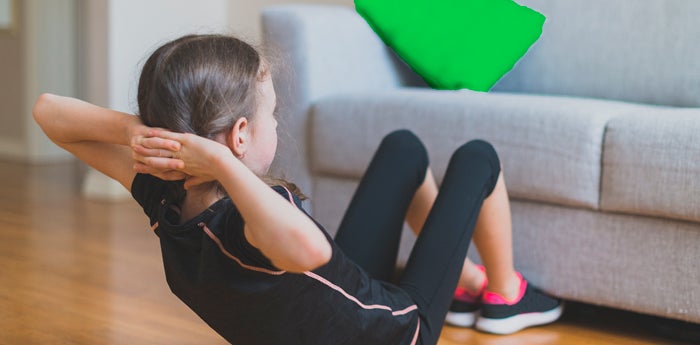 Niña haciendo abdominales en casa con ayuda de un sofá