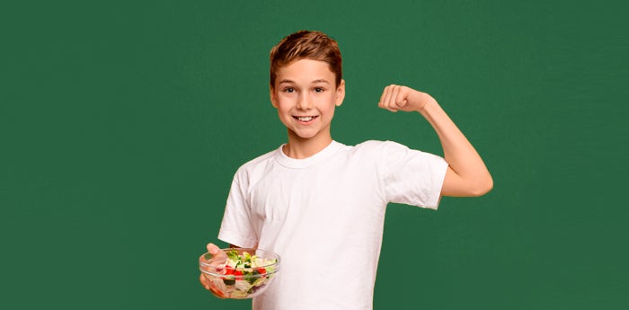 Niño alegre mostrando sus músculos y sosteniendo un plato de verduras