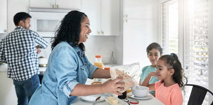  mamá sirve a su hija cereal en una taza mientras desayunan en familia. 