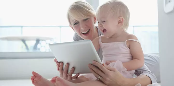 Mamá e hija riendo y observando contenido en una tableta virtual
