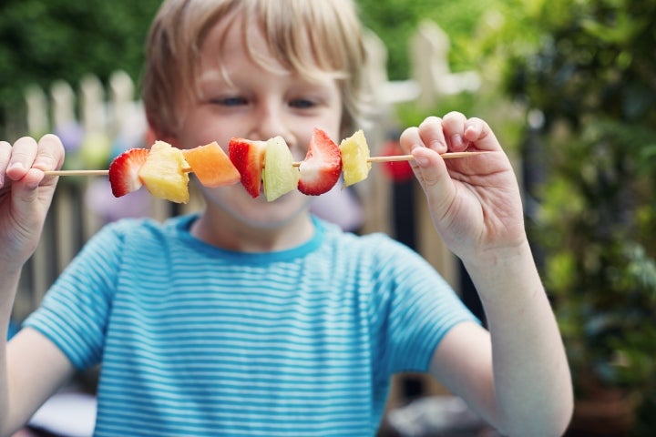 Brochetas de frutas que está comiendo un niño