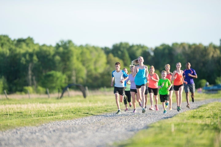 Grupo de niños y adultos corriendo juntos en un entrenamiento de atletismo al aire libre.