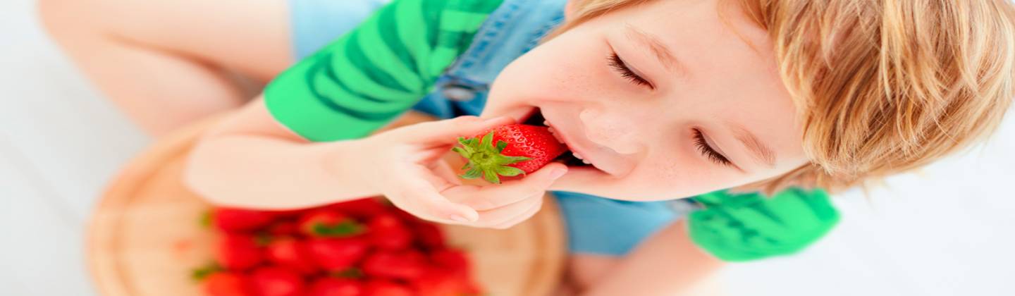 Niño rubio feliz comiendo fresas