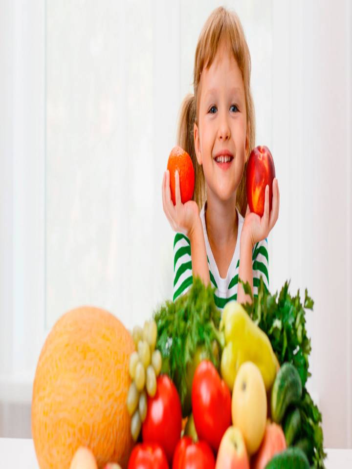 Niña sonriente junto a diversas frutas y verduras